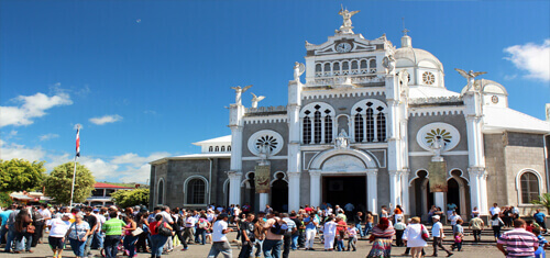 ). Picture a church in Costa Rica representing the vacation opportunities available for patients having plastic surgery in Costa Rica.  The picture shows many tourists and sightseers outside of the church.