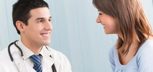 Picture of a doctor consulting with a female patient.  The doctor is wearing a white coat with a stethoscope around his neck and is smiling at the patient.