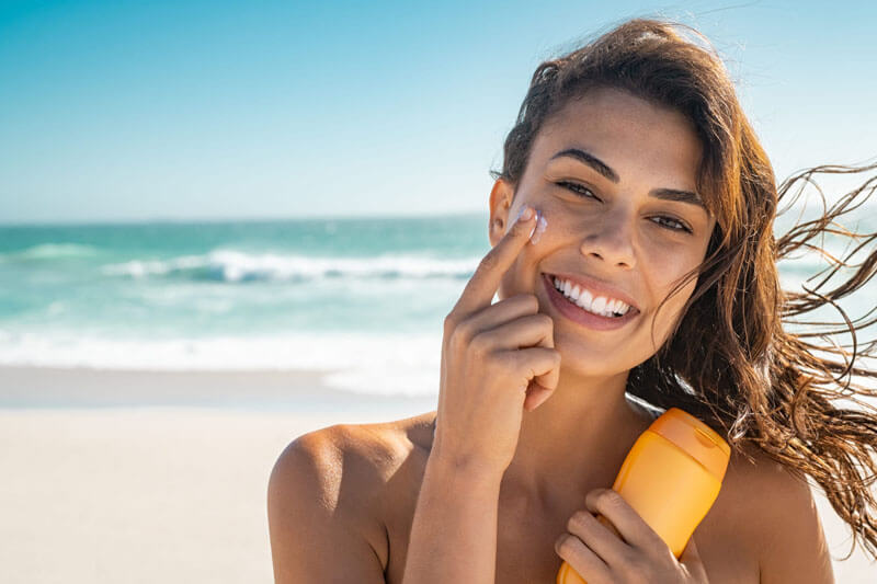 Picture of a smiling woman, happy with her nose surgery she had at Top Plastic Surgeons U.K.  The woman has long brown hair and is standing on a sandy Costa Rican beach with the ocean in the background.