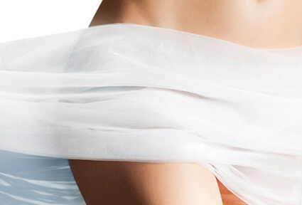 Picture of a woman standing with a flowing sheet around her body and happy with her perfect pubic liposuction procedure she had at Top Plastic Surgeons in beautiful San Jose, Costa Rica.  She is facing slightly away from the camera and the sheet is white.