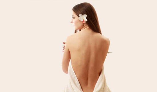 Picture of a woman sitting with her back to the camera and happy with her perfect back liposuction procedure she had at Top Plastic Surgeons in beautiful San Jose, Costa Rica.  The woman has a white towel draped around her.
