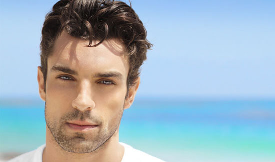 Picture of a man, facing the camera and happy with his perfect hair transplant procedure he had at Top Plastic Surgeons in beautiful San Jose, Costa Rica.  The man has a white t-shirt on and has a blue ocean as a backdrop.